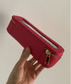 Red rectangular pouch with gold zipper held by a hand against a beige background